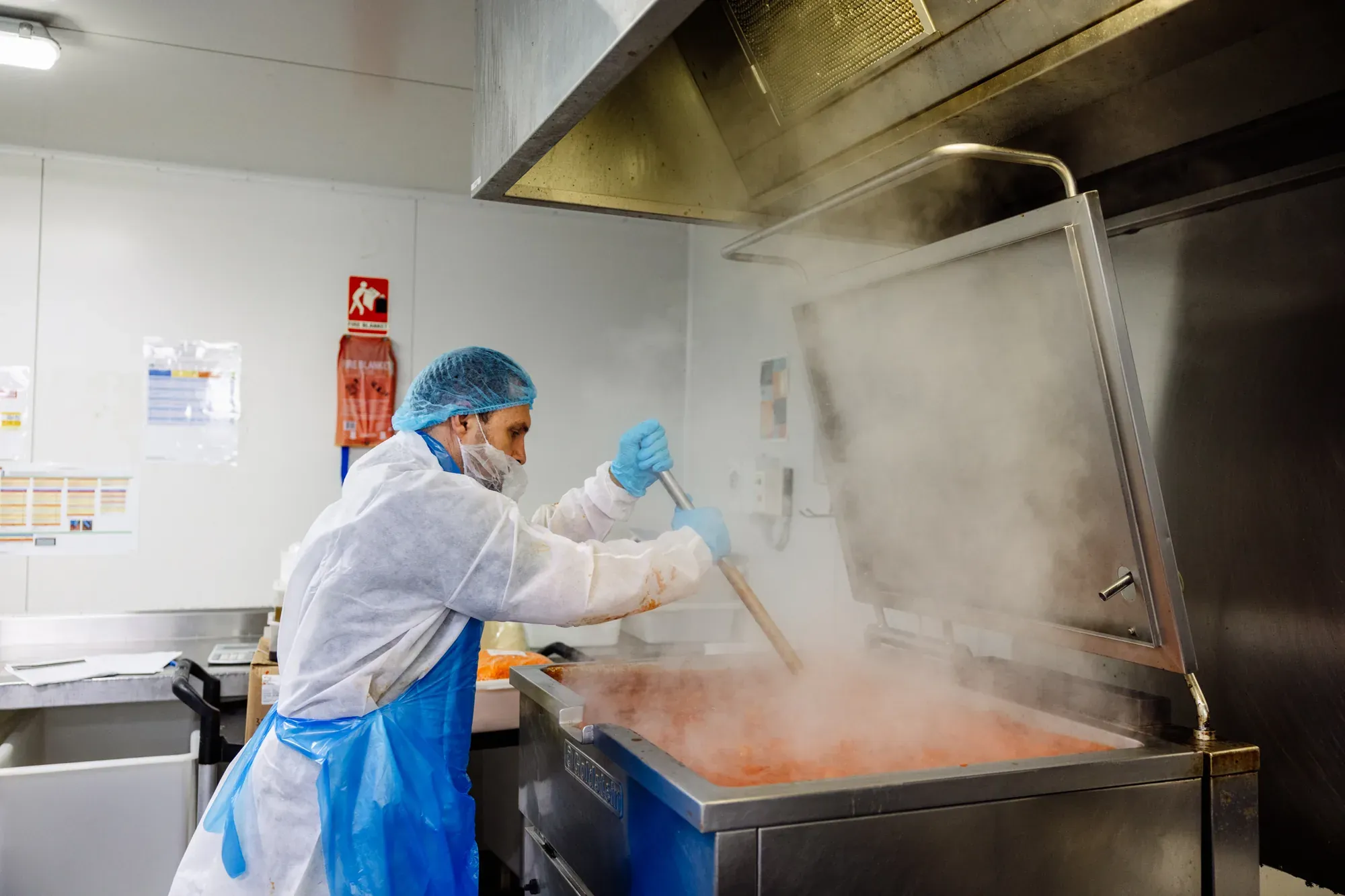 A cook in protective clothing stirring a steaming vat of sauce in the Cucina Classica kitchen