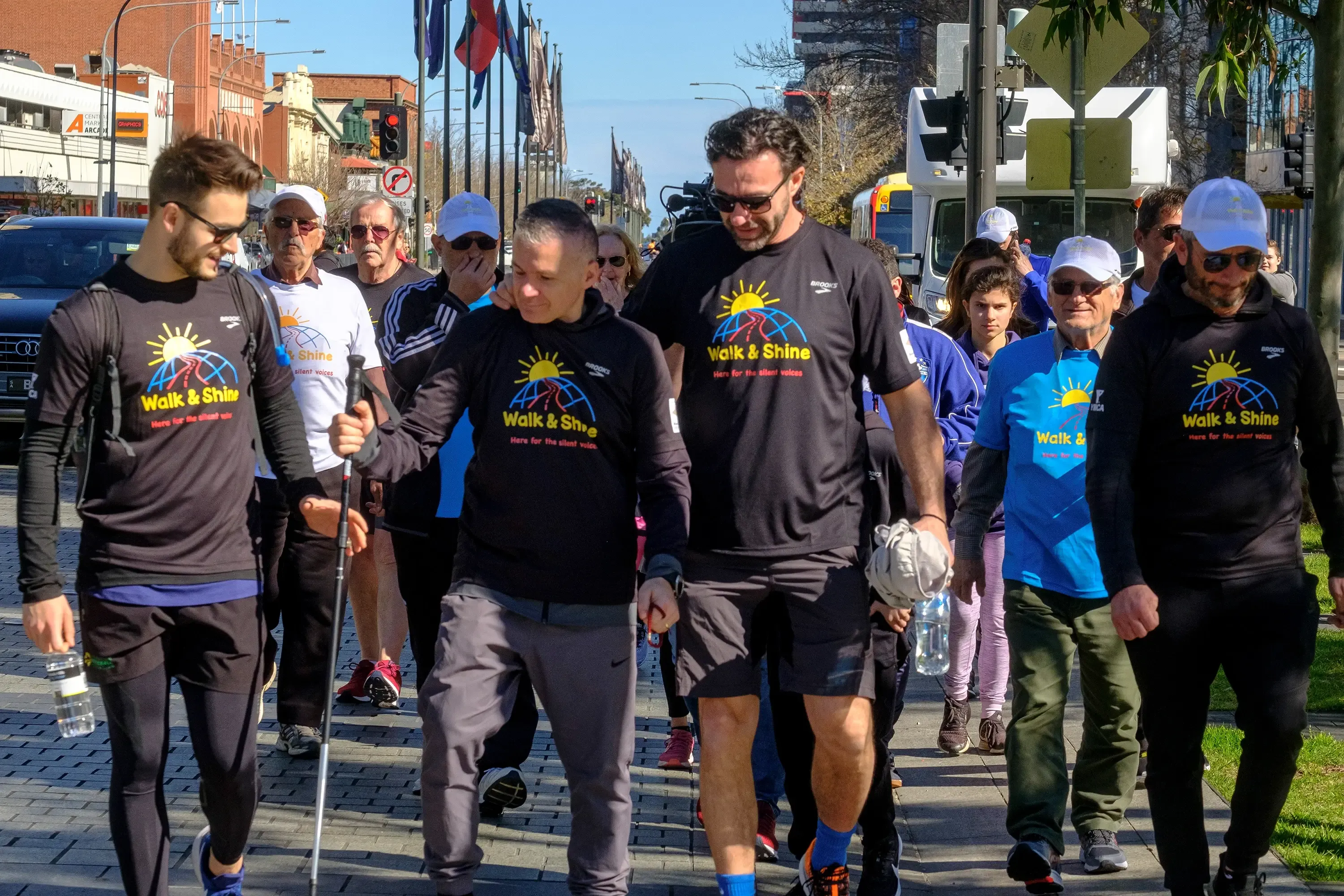 A crowd of Walk and Shine participants walking through the city, with a television camera truck following